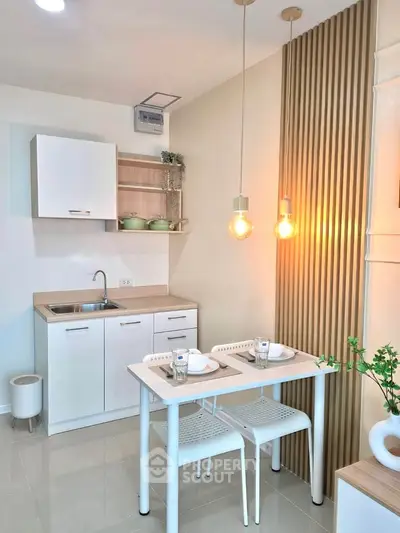 Modern kitchen with sleek white cabinets, compact dining area, and stylish pendant lighting.