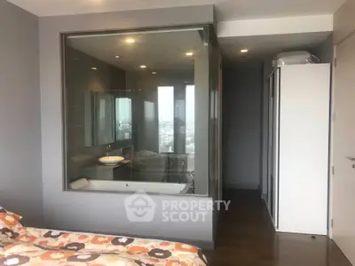 Modern bedroom with glass-walled bathroom and city view, featuring sleek design and cozy ambiance.