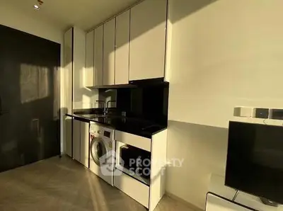 Modern kitchen with sleek cabinetry and built-in washing machine in a sunlit apartment.