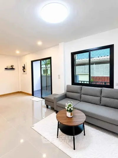 Modern living room with sleek gray sofa and stylish coffee table, featuring large windows and a bright ambiance.