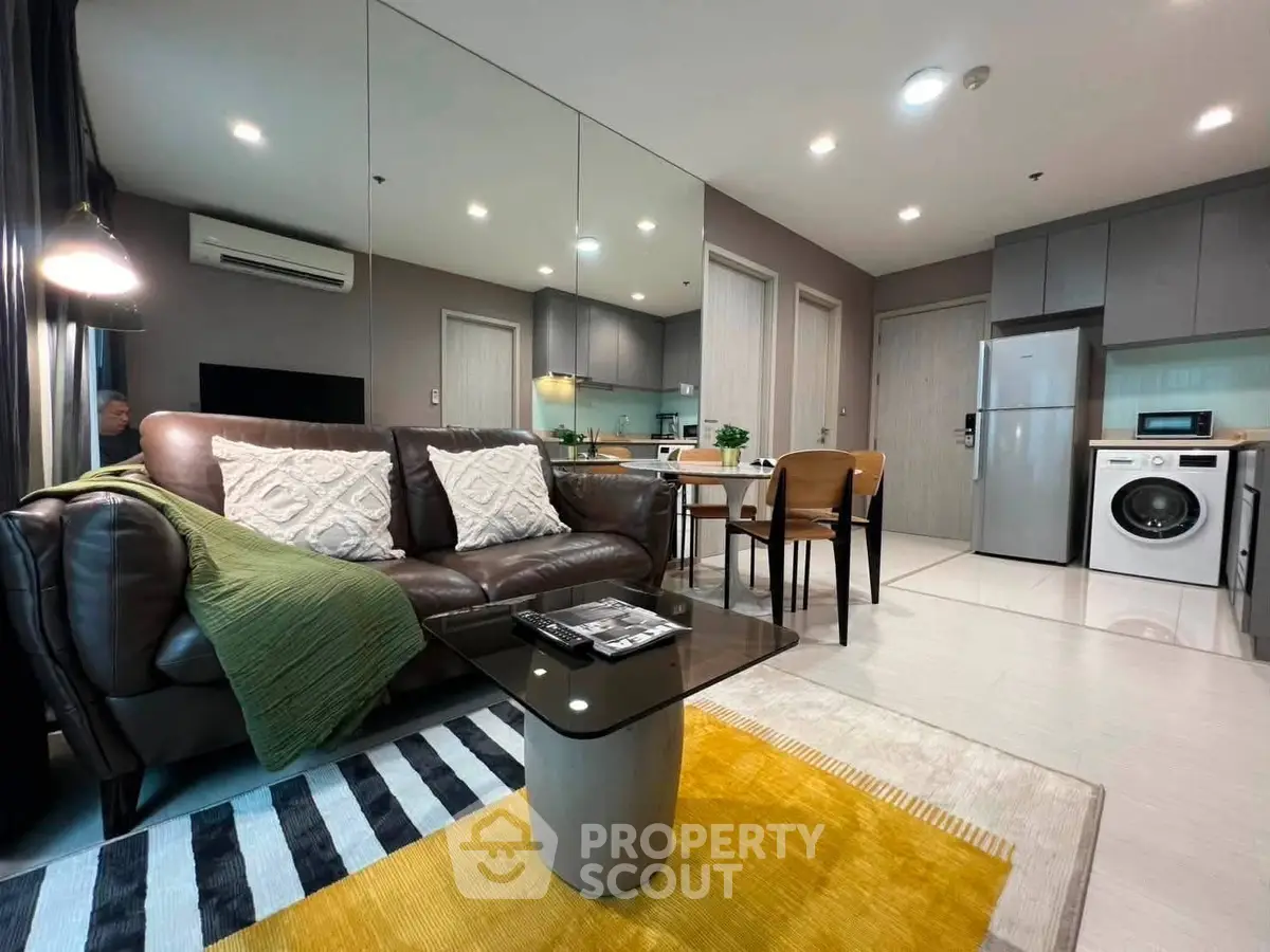 Modern living room with stylish furniture, open kitchen, and in-unit washer in a contemporary apartment.