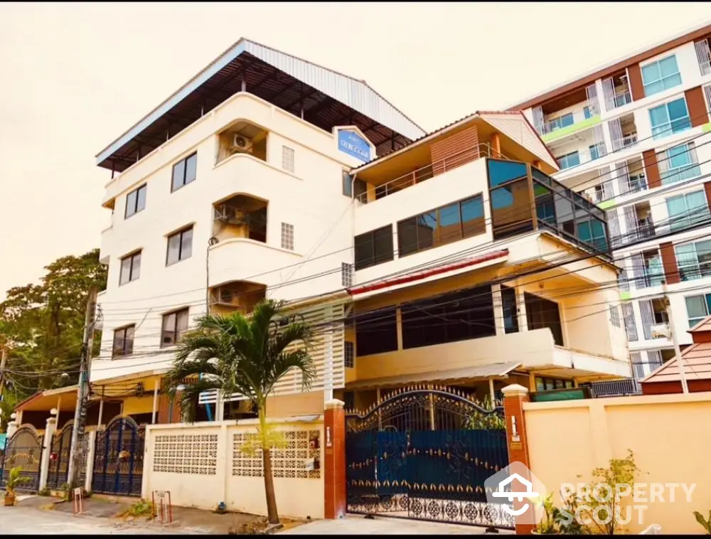 Charming multi-story residential building with gated entrance and palm tree in urban setting.