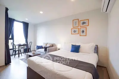 Modern bedroom with cozy decor and natural light, featuring a stylish seating area and elegant furnishings.