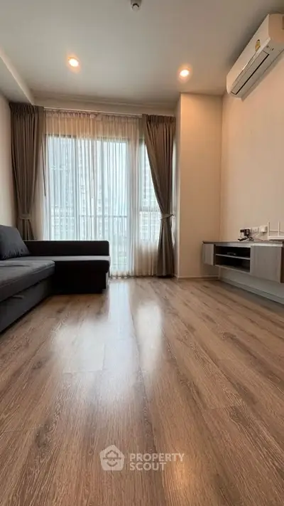 Modern living room with hardwood floors, large window, and air conditioning unit.