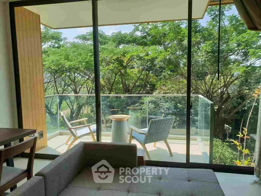 Serene living room with large glass doors opening to a lush balcony view, modern furniture, and abundant natural light.