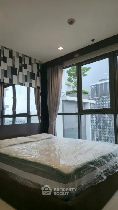 Modern bedroom with large windows and city view, featuring stylish decor and natural light.