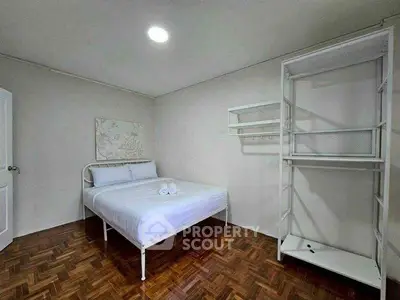 Minimalist bedroom with white metal bed frame and open wardrobe on wooden flooring.