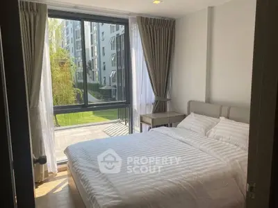 Cozy bedroom with large window offering a serene garden view in modern apartment.