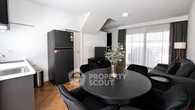 Modern living room with sleek black furniture and open kitchen layout, featuring a stylish dining area and large windows.