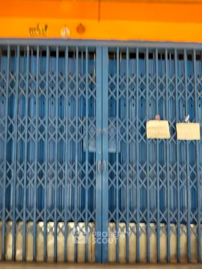 Closed blue metal gate of a commercial property with orange wall, ideal for retail or storage.