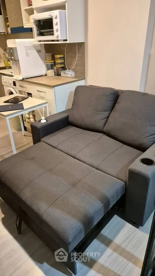Modern compact living room with stylish gray sofa bed and sleek kitchen appliances.