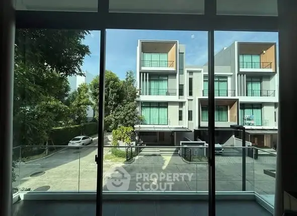 Modern townhouse complex with large windows and balconies, viewed from inside through glass doors.