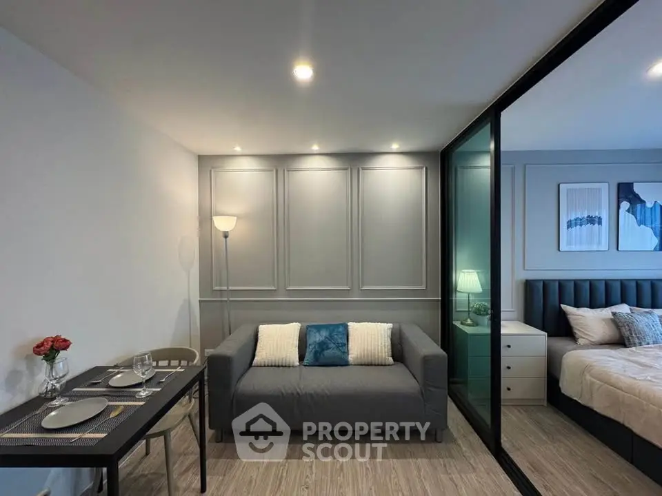 Modern living room with cozy sofa and elegant bedroom separated by glass partition.