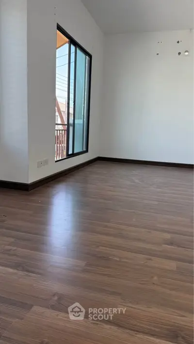 Spacious empty room with wooden flooring and large window