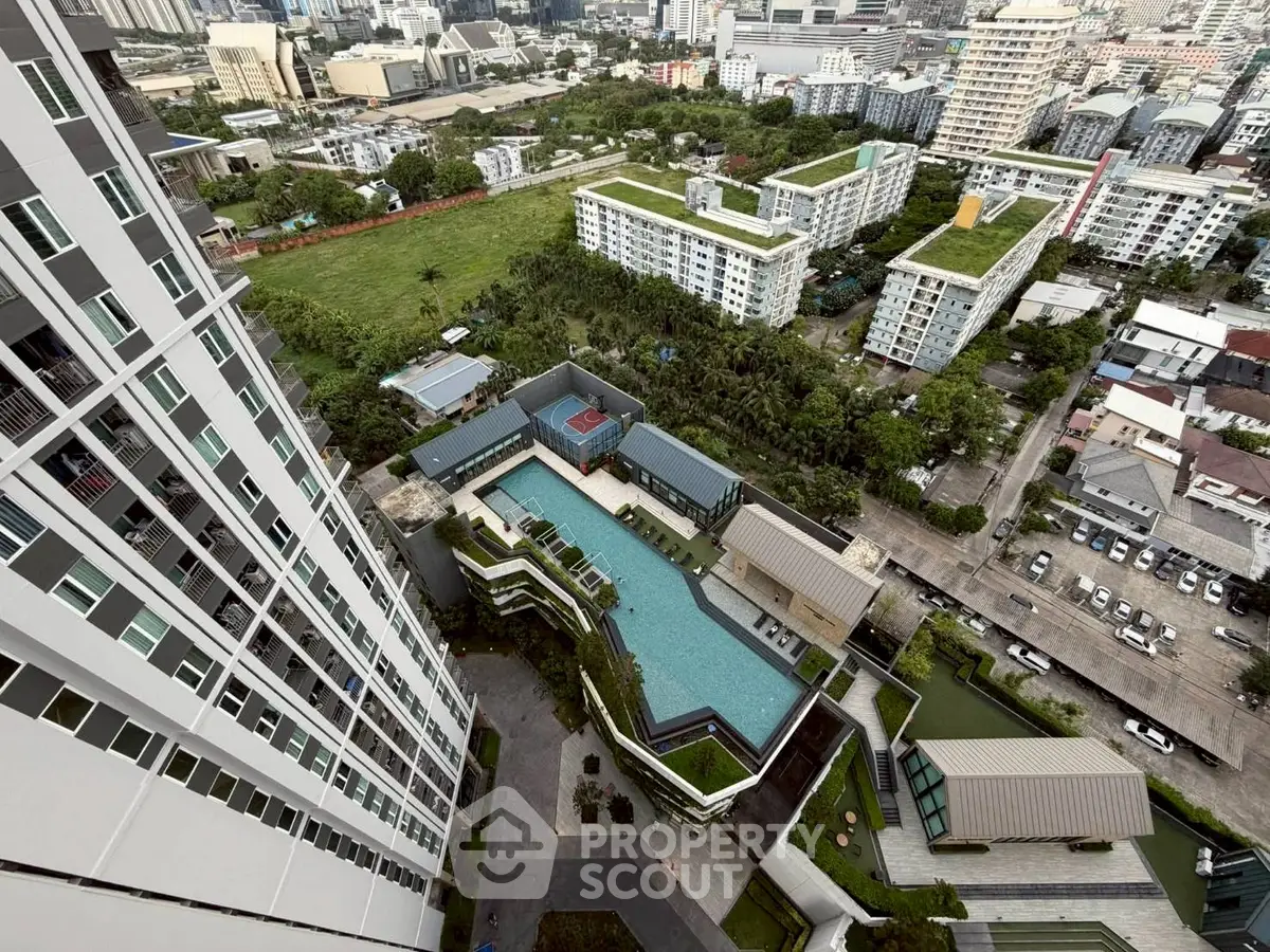 Stunning aerial view of modern high-rise building with luxurious pool and lush green surroundings in urban setting.