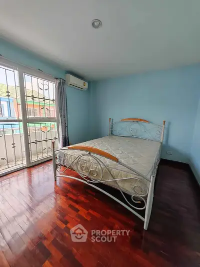 Cozy bedroom with elegant metal bed frame and hardwood floors, featuring a small balcony with natural light.