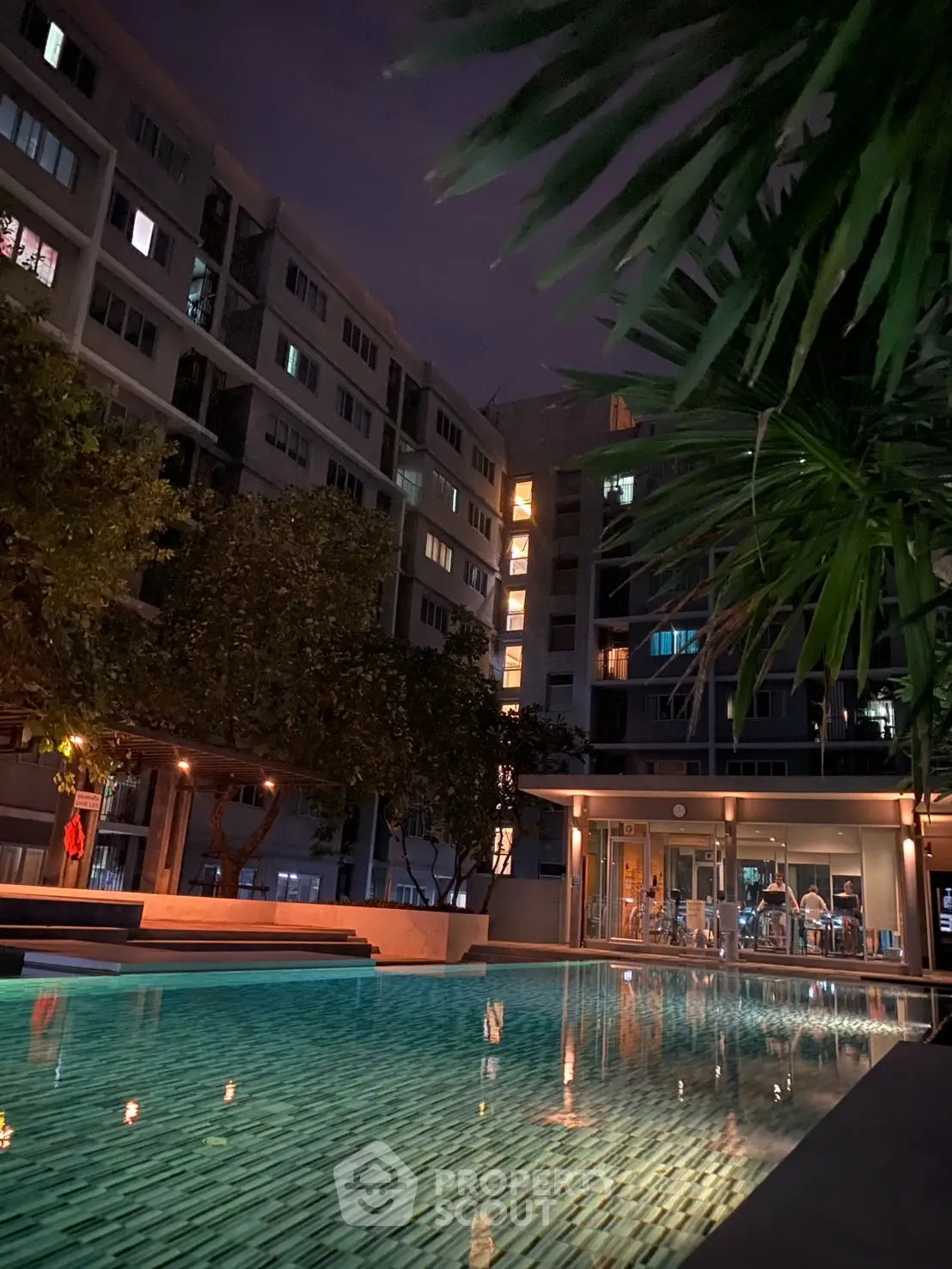 Luxurious residential building with illuminated pool and lush greenery at night