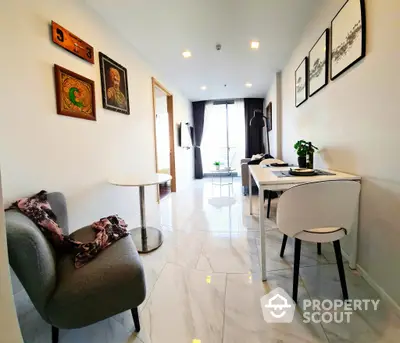 Elegant modern living space with polished marble floors, cozy grey armchairs, and tasteful wall art, leading to a bright dining area with natural light.