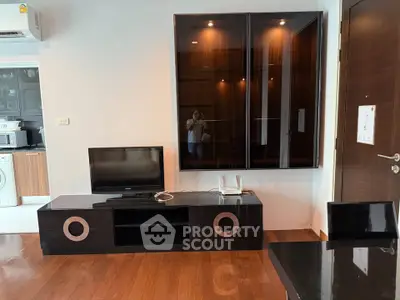 Modern living room with sleek black furniture and wooden flooring, featuring a compact TV setup and stylish cabinetry.