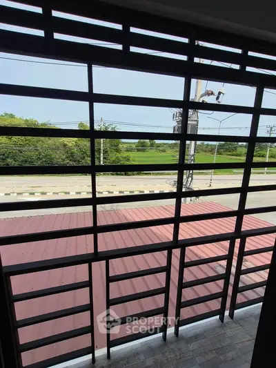 Spacious balcony with metal railing offering a serene view of lush greenery and a quiet road.