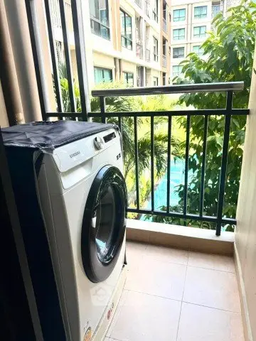 Charming balcony with washing machine overlooking lush greenery and pool view.