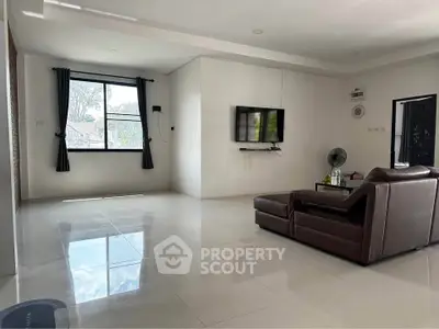 Spacious modern living room with sleek leather sofa and wall-mounted TV, featuring large window for natural light.
