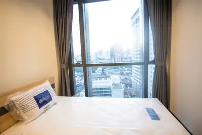 Modern bedroom with city view from large window, featuring a comfortable bed and elegant curtains.