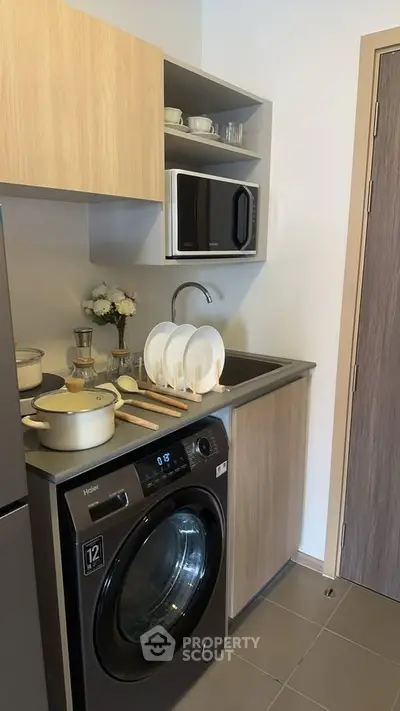 Modern compact kitchen with washing machine and microwave in stylish apartment.