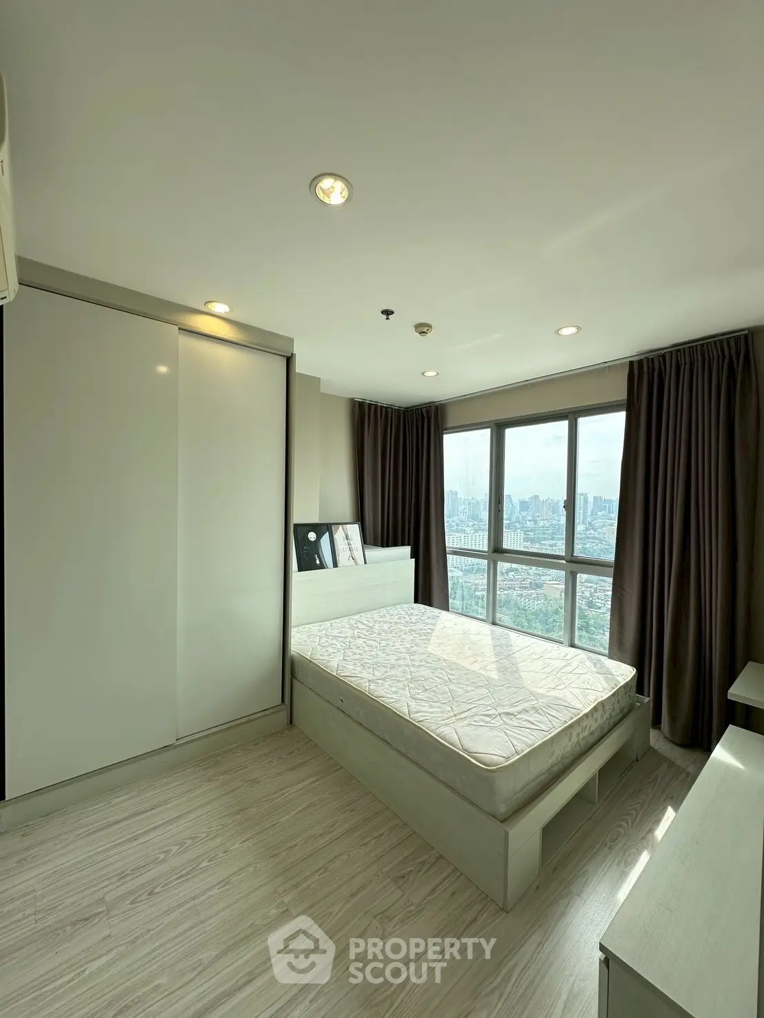 Modern bedroom with large window offering stunning city views, featuring sleek furniture and ample natural light.