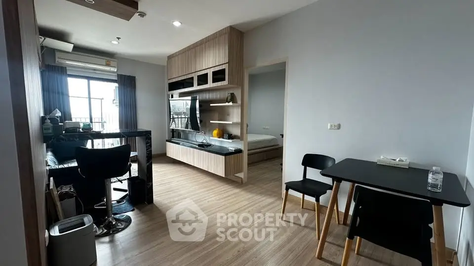 Modern open-plan living room with dining area and bedroom view, featuring sleek furniture and natural light.