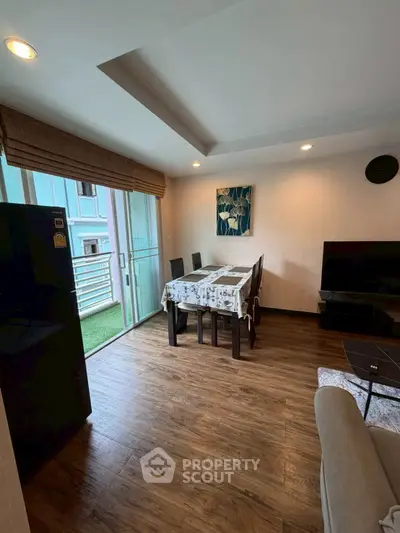 Cozy living room with dining area and balcony access, featuring wooden flooring and modern decor.