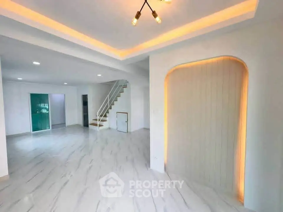 Spacious modern living room with elegant lighting and staircase, perfect for stylish living.