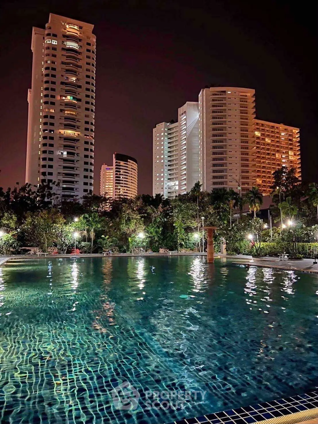 Stunning night view of luxury high-rise buildings with illuminated swimming pool in foreground.