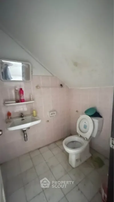 Compact bathroom with sloped ceiling and basic fixtures in need of renovation.
