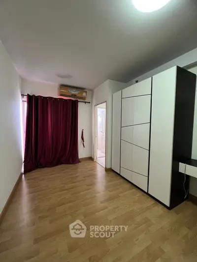 Spacious bedroom with wooden flooring and large wardrobe, featuring elegant maroon curtains for a cozy ambiance.