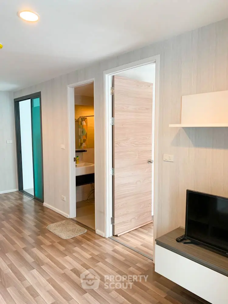 Modern apartment interior with open door to bathroom and sleek wooden flooring.