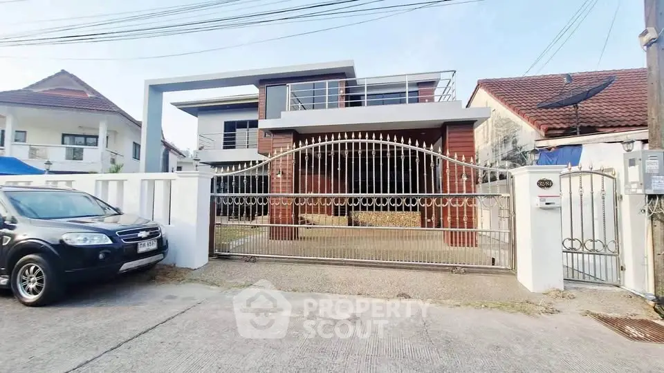 Modern two-story house with gated entrance and driveway, featuring contemporary architecture and spacious outdoor area.
