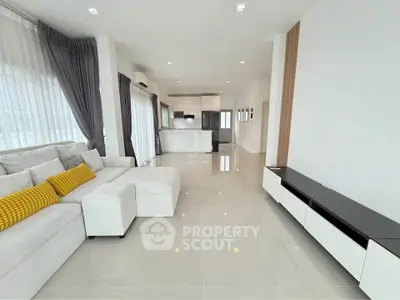 Spacious modern living room with open kitchen, sleek furniture, and large windows for natural light.