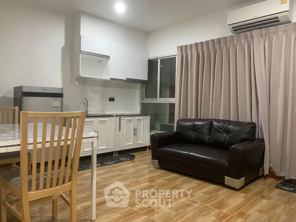 Modern living room with sleek kitchen, featuring a black leather sofa and wooden dining set, perfect for cozy gatherings.