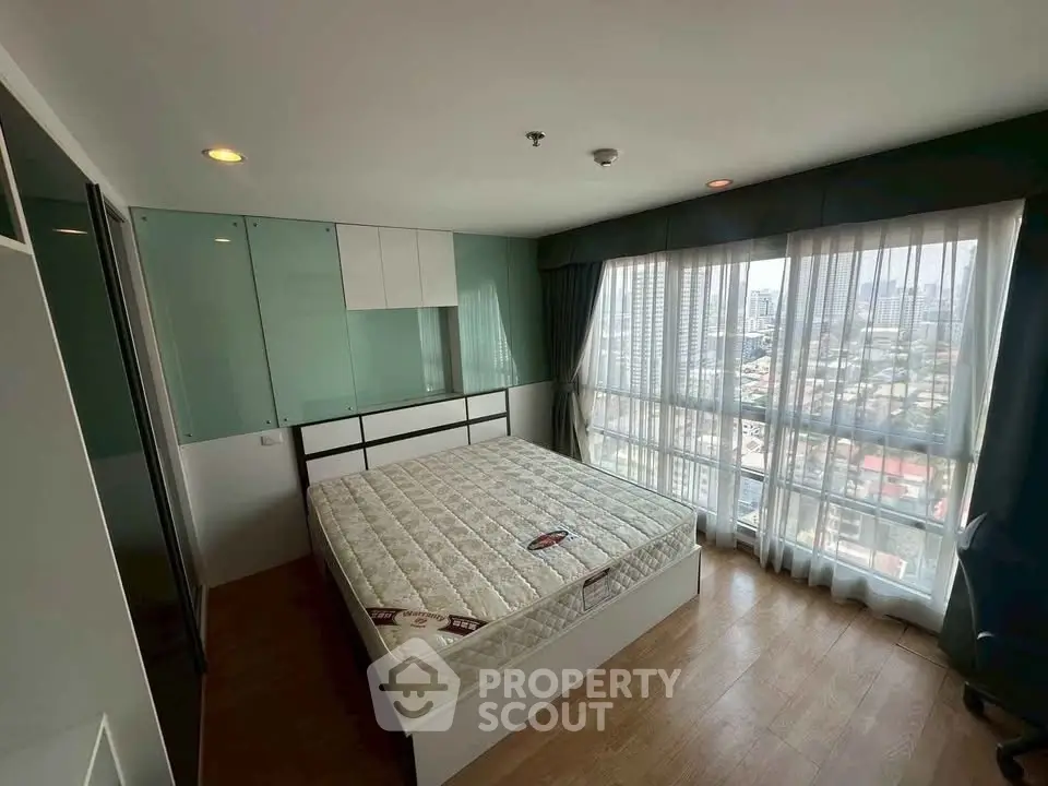 Spacious bedroom with large windows offering stunning city views, featuring a comfortable bed and modern decor.