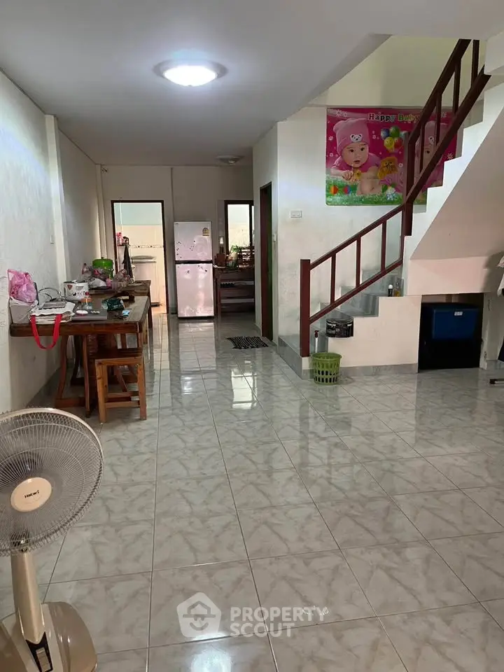 Spacious open-plan living area with tiled flooring and staircase, featuring a dining table and kitchen access.