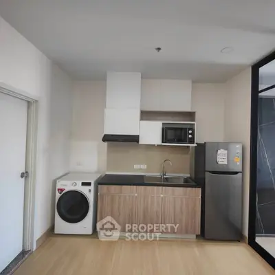 Modern kitchen with washing machine, microwave, and fridge in compact layout.