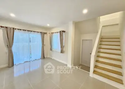 Spacious living room with elegant staircase and large windows for natural light.
