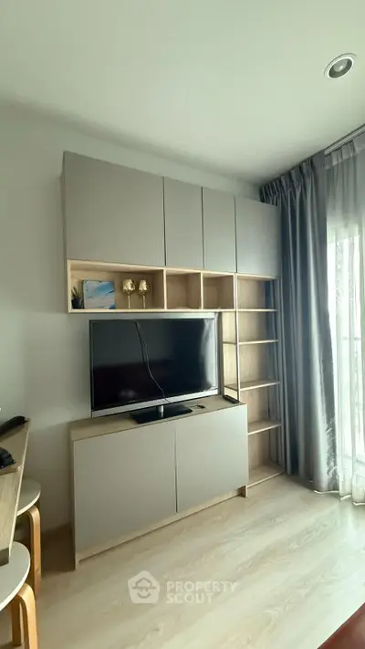 Modern living room with sleek TV unit and natural light from large window.