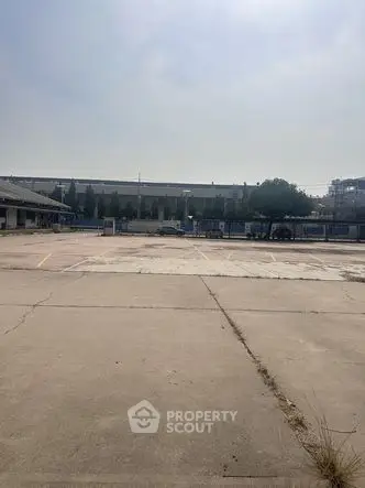 Spacious parking lot with clear sky and industrial surroundings, ideal for commercial use.