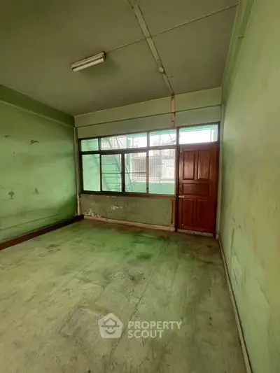 Spacious room with large window and wooden door, ideal for renovation or customization.