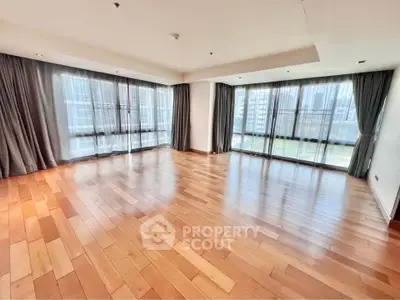 Spacious corner unit living room with large windows and hardwood floors in a modern apartment.