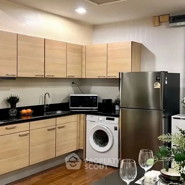 Modern kitchen with sleek appliances and wooden cabinets, featuring a washing machine and stainless steel fridge.