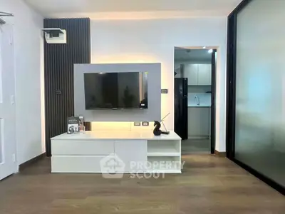 Modern living room with sleek TV unit and open kitchen view, featuring stylish decor and warm lighting.