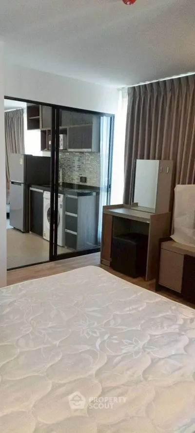 Modern bedroom with view into sleek kitchen featuring washing machine and fridge